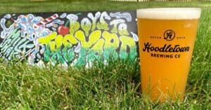 IPA beer in a Hoodletown pint glass sitting in the grass with a sign that says "Boys to the Yard IPA"