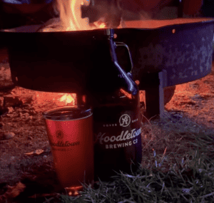 Hoodletown's Station 2 Smoky Lager in a pint glass with a growler next to it posed in front of a fire pit.